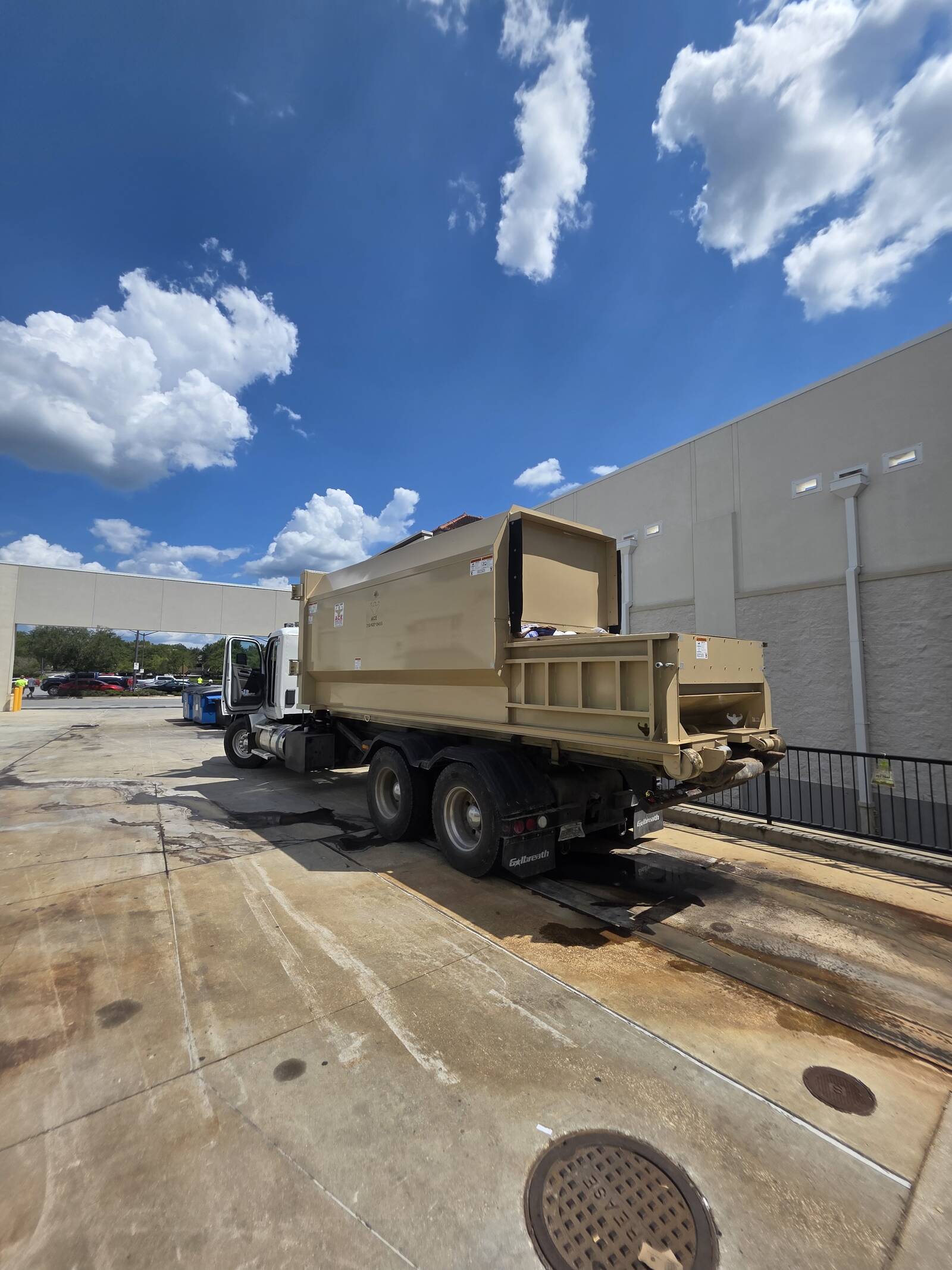 Commercial compactor receiver box loaded on a Muckpro roll-off truck behind a retail store