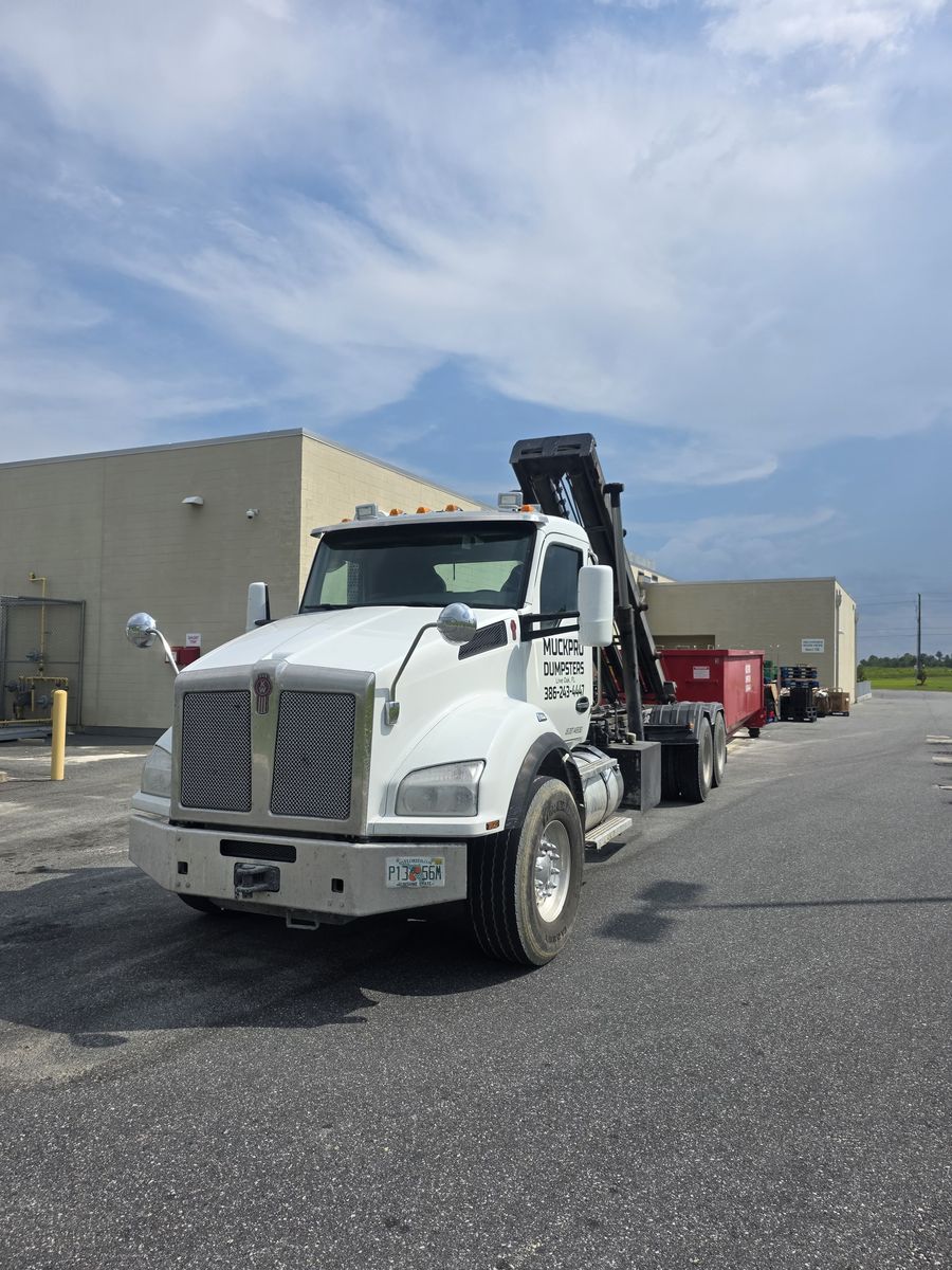 Muckpro Kenworth roll-off truck delivering a dumpster to a Live Oak commercial site