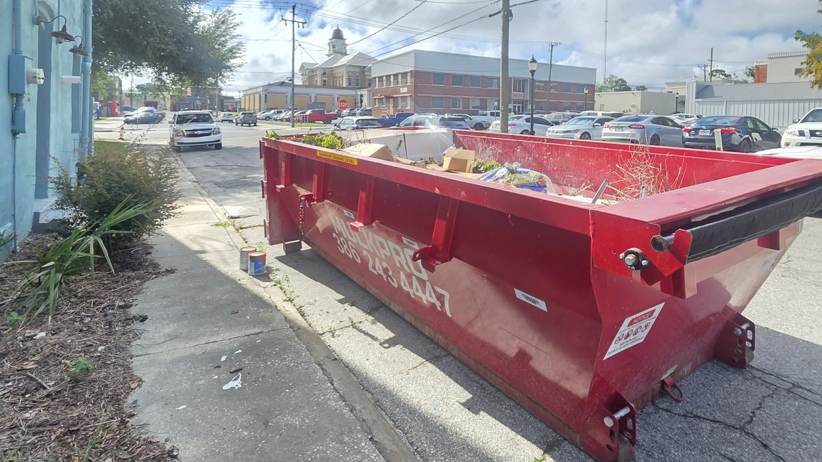 Muckpro 15-yard dumpster set curbside in downtown Live Oak, FL with the restored Suwannee County Courthouse dome behind it