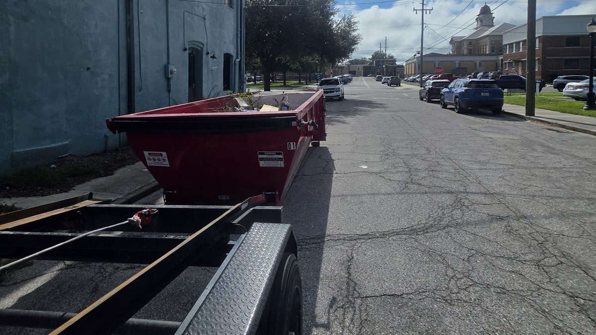Muckpro trailer roll-off delivering a dumpster on a downtown Live Oak, FL street near the Suwannee County Courthouse