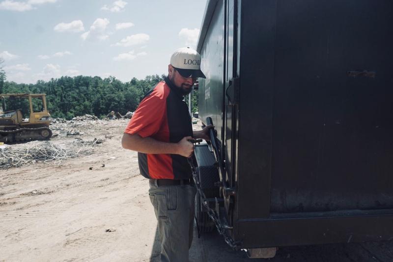 Muckpro operator chaining a loaded roll-off dumpster for haul-off